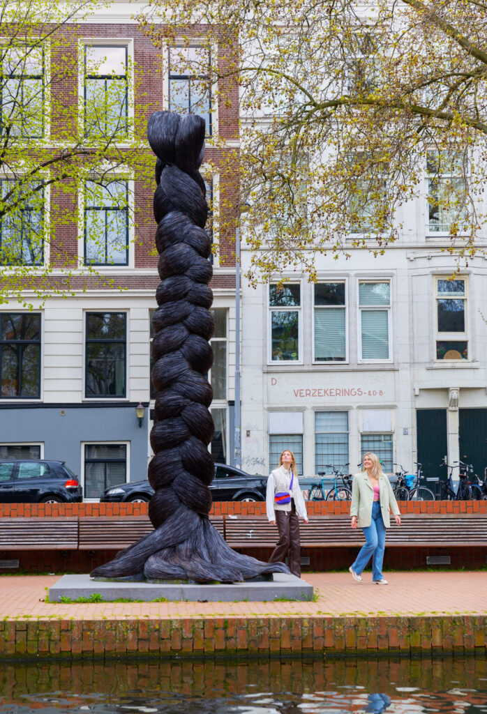 De vlecht is een stalen sculptuur uit 2020 van beeldhouwer Kalliopi Lemos, die bekendstaat om haar grootschalige openbare installaties. De rechtopstaande vlecht van donkerbruin haar heeft een lengte van 6,5 meter hoog. De vlecht maakt deel uit van haar beeldenserie Tools of Endearment en gaat over de rol van vrouwelijkheid in de moderne samenleving.